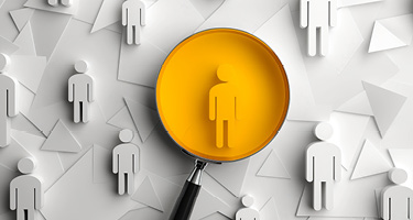 Magnifying glass focusing on a single yellow human figure among gray human cutouts.