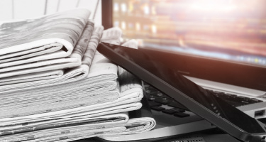 A stack of newspapers next to an open laptop, symbolizing the blend of traditional and digital media