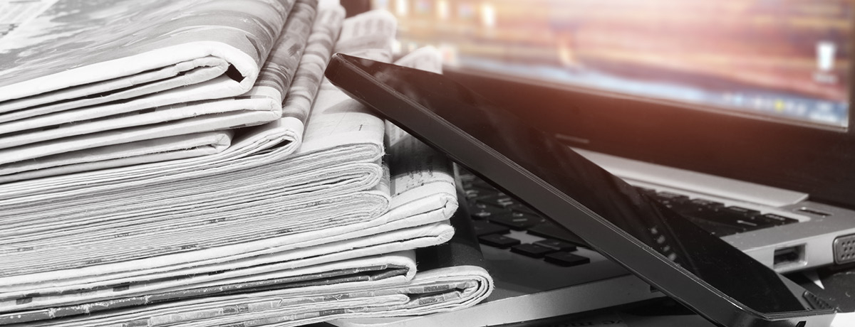 A stack of newspapers next to an open laptop, symbolizing the blend of traditional and digital media