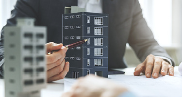 Unseen figure with pen points to apartment building model