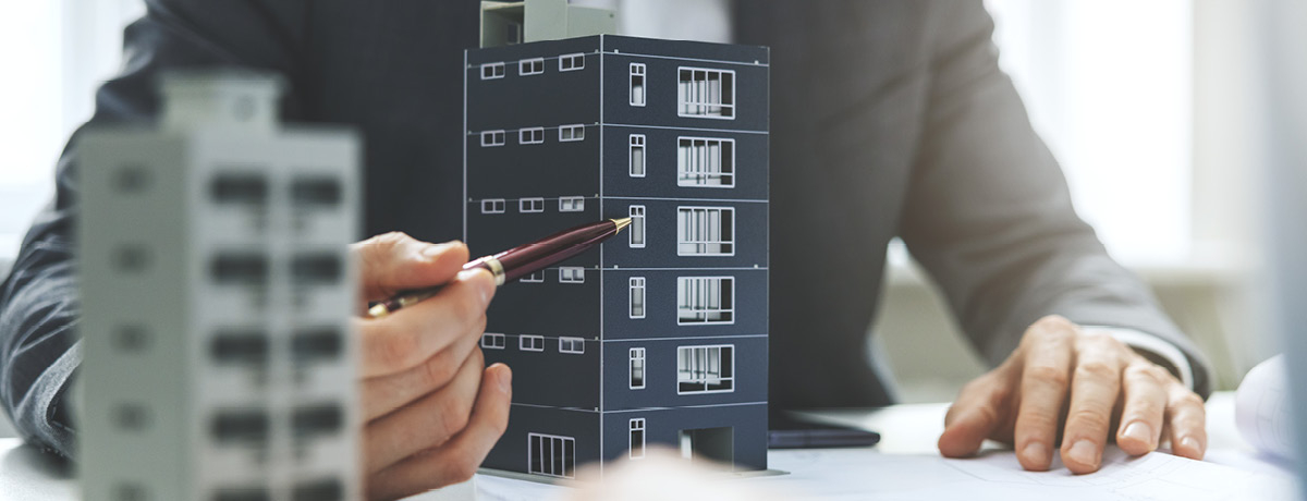 Unseen figure with pen points to apartment building model