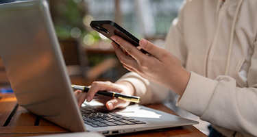 Person at a computer holding a phone and pen