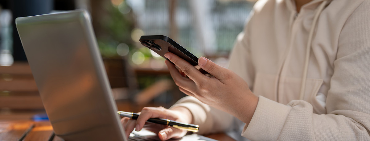 Person at a computer holding a phone and pen