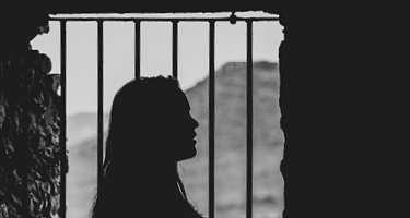 Black silhouette of woman standing near cell bars 