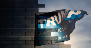 Brick wall half destroyed with open sky on the other side and Trump flag waving