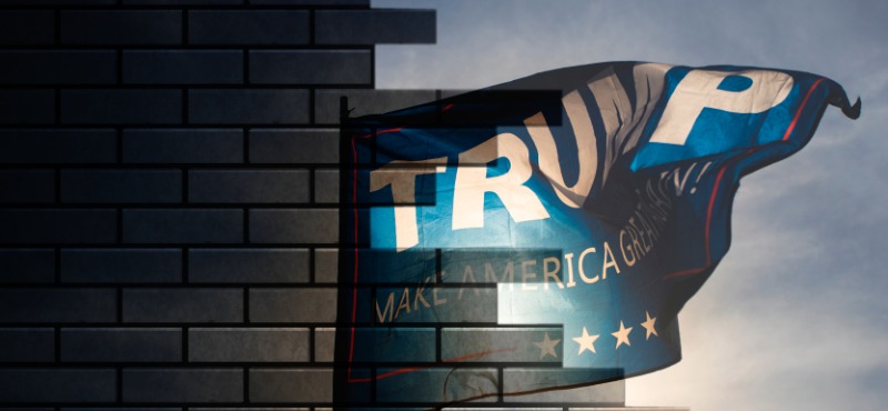 Brick wall half destroyed with open sky on the other side and Trump flag waving