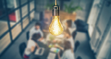 Lightbulb glowing over meeting room of people