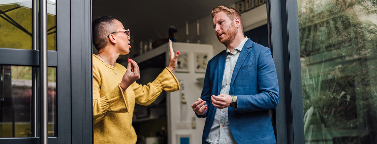 Spouses standing in doorway of home having argument