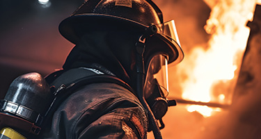 Firefighter stands with their back turned with flames in the background