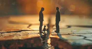 Miniature figures of two people standing apart with a child figure between them on a cracked surface