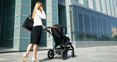 Woman in business attire pushing stroller takes a phone call