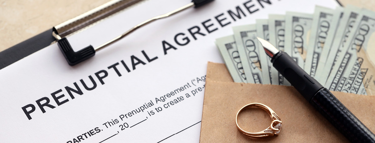 A wedding ring and envelope of money on top of a prenuptial agreement