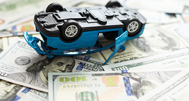 Toy car laying upside down on pile of money