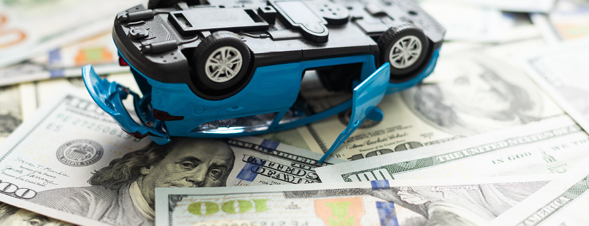 Toy car laying upside down on pile of money