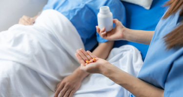 Medical professional holds pill bottle standing over patient in bed