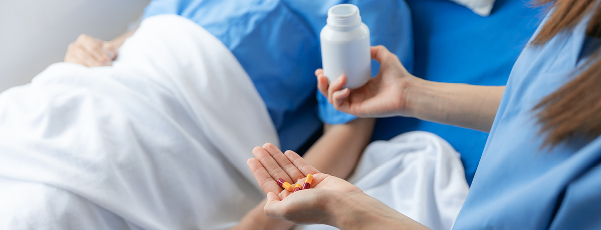 Medical professional holds pill bottle standing over patient in bed