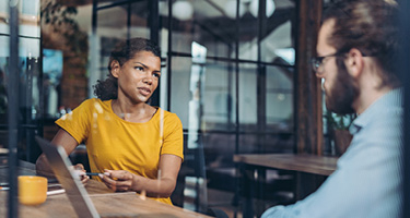 Woman in yellow shirt talking with man in blue shirt at desk
