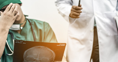 Doctor with hand on face reviewing scan with another doctor in backdrop