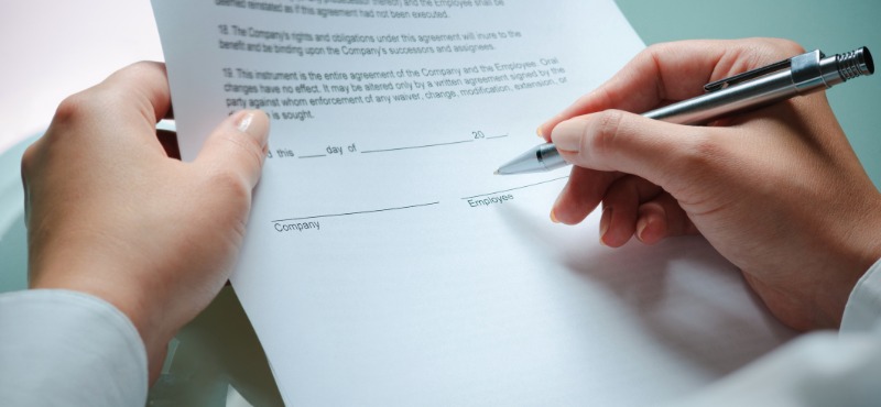 Woman signs noncompete agreement with silver pen while wearing a suit