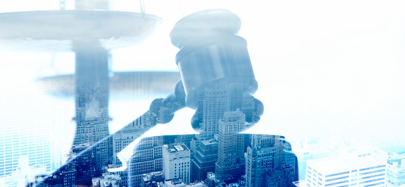 Judge’s wooden gavel striking a sound block, overlaid with faint courthouse columns