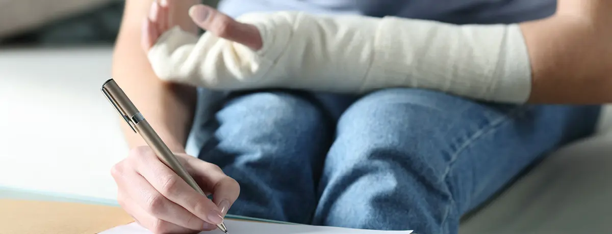 Person writing notes on paper with pen reviewing personal injury claim documentation