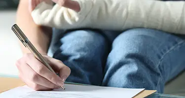 Person writing notes on paper with pen reviewing personal injury claim documentation