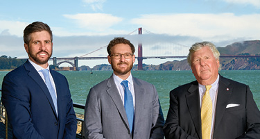 Three lawyers in suits pose in front of a bridge