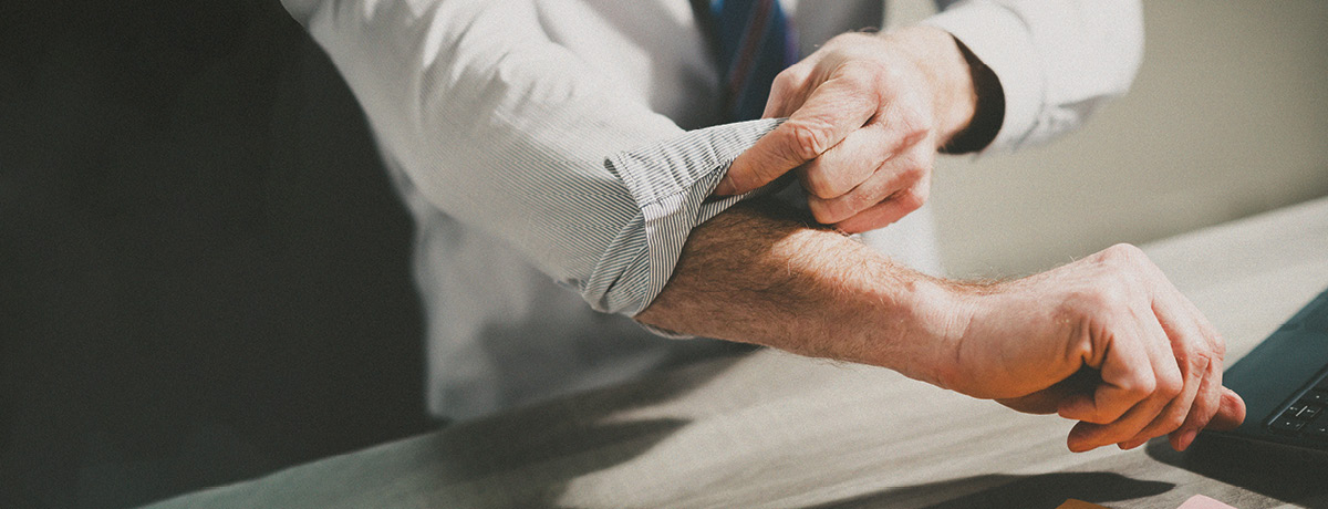 Unseen figure wearing suit rolls up sleeves
