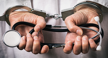 Doctor with hands behind back in handcuffs holding stethoscope