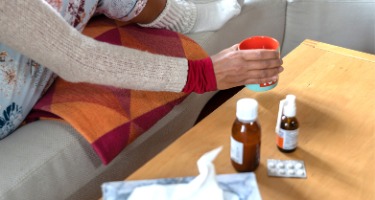 Woman sick from Coronavirus reaches for cold medicine on a table 