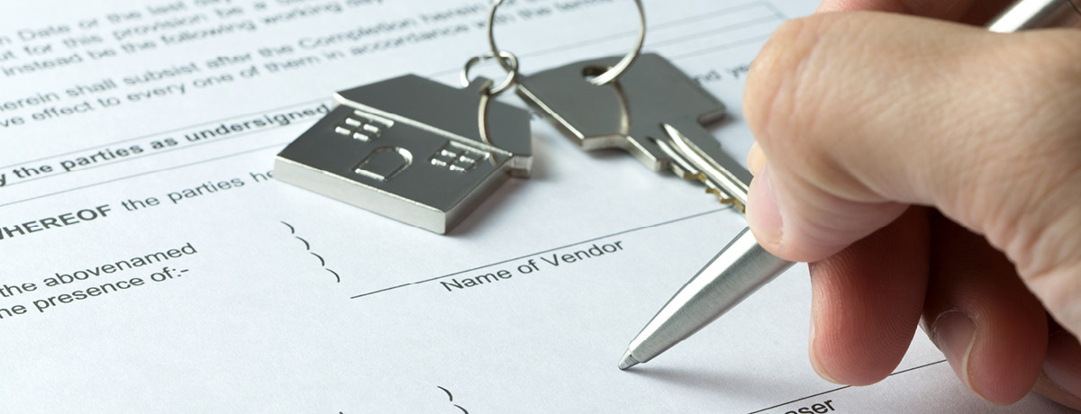 Individual signing a document with house keys in background