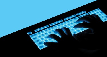 Hands typing on blue, light up keyboard