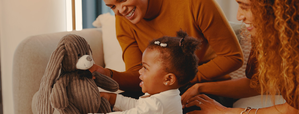 Child holding a teddy bear with two women sitting with her