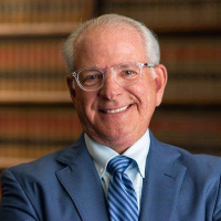 Headshot of man in blue suit with grey hair and glasses