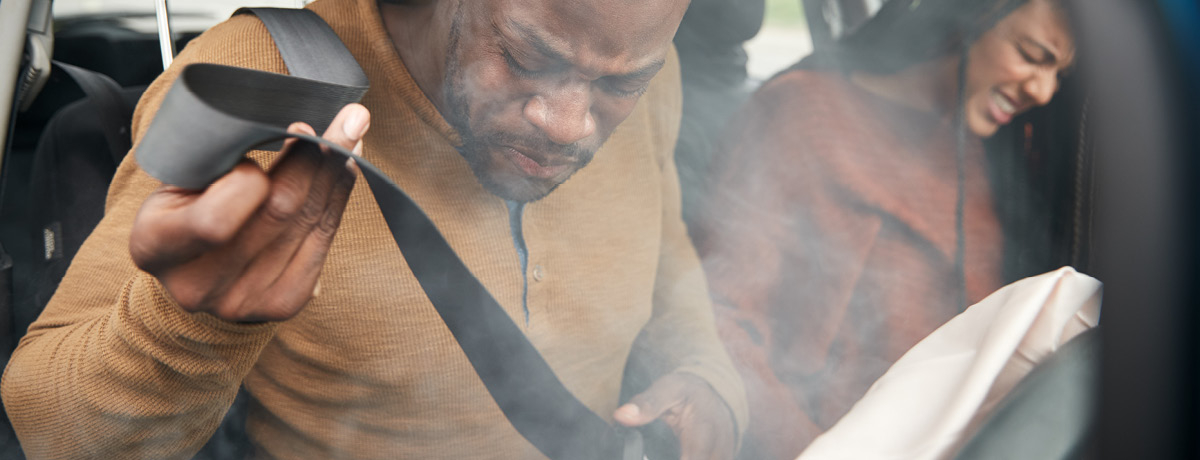 Man and woman in car with airbags deployed and smoke coming from dash