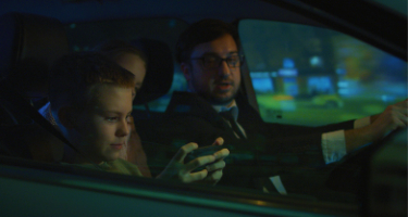 Family sitting in a car driving somewhere with son on his phone and man driving his car