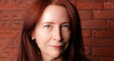 Headshot of female lawyer with red hair standing in front of brick wall