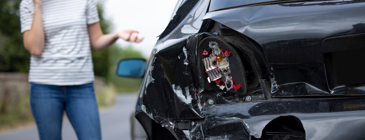Woman on phone surveys damage to vehicle
