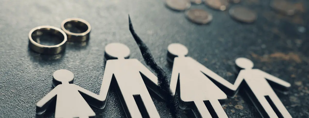 Paper cutout family figures split down the middle by a crack, with two wedding ring.