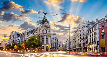 Tall buildings and rushing traffic against clouds and sun in sky