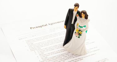 Bride and groom figurines standing on prenuptial agreement papers