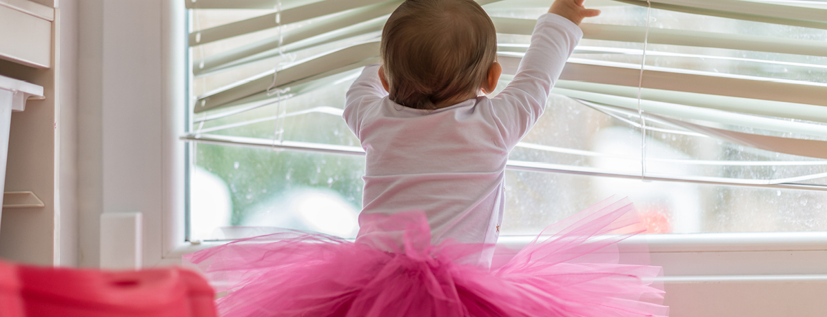 Baby wearing pink tutu playing with window blinds