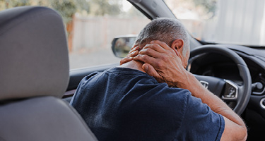 Man at steering wheel leaning forward grasping sore neck