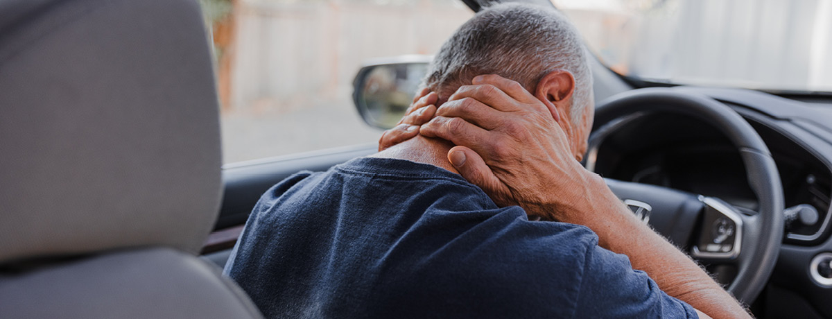Man at steering wheel leaning forward grasping sore neck