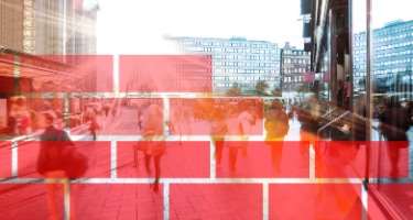 Red wall being built brick by brick with city behind it