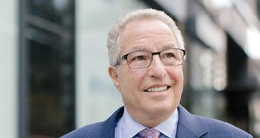 Headshot of man in light blue suit standing outside