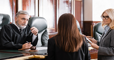Male judge in court room talking with two female lawyers