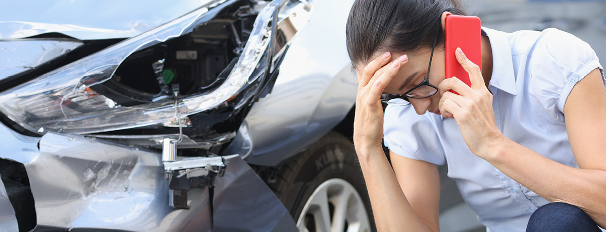 Woman on phone call with damaged car in the background