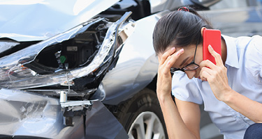 Woman on phone call with damaged car in the background