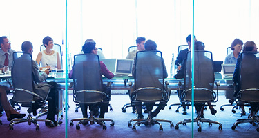 Several people sitting in chairs around boardroom table